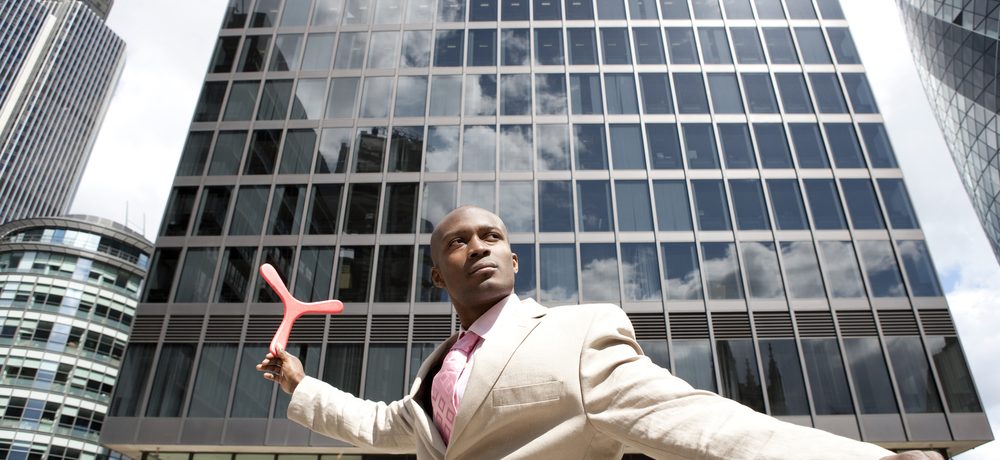 A young African American male about to throw a boomerang outside a modern office