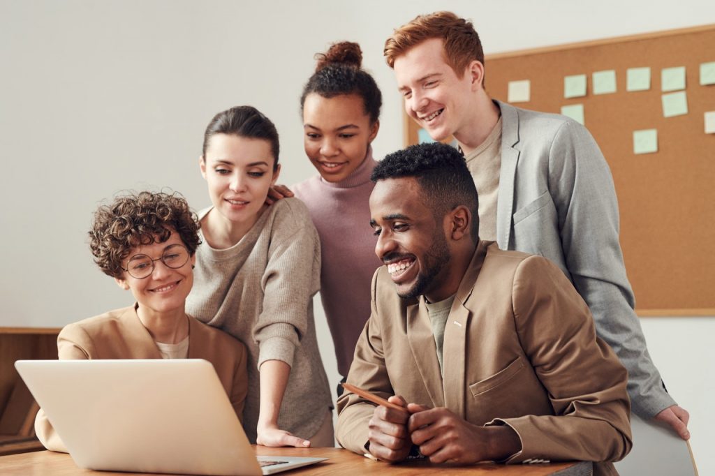 Group of five people smiling around laptop.
