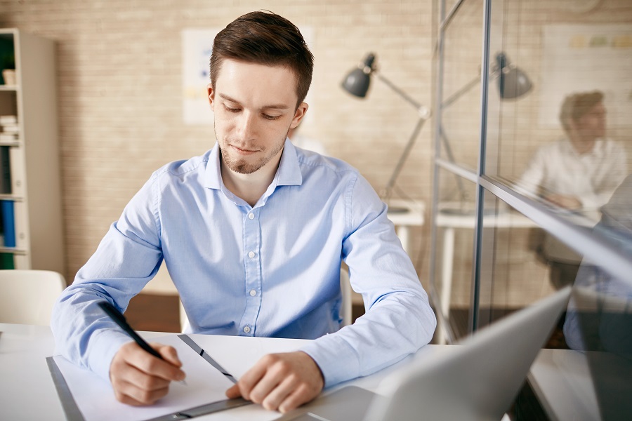 White collar worker sitting by desk and making notes