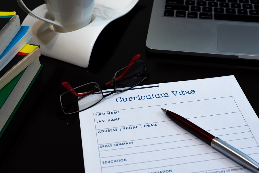 Close up images of a desk with a CV, glasses, pen & laptop placed