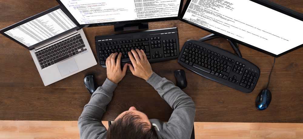 Young Man working from 2 Computers And Laptop At Desk